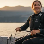 Velista mentre timona una piccola barca a vela su un lago tranquillo al tramonto.