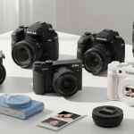 Tavolo con diverse fotocamere digitali: una reflex, una mirrorless, una compatta e una fotocamera istantanea.