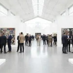 Una tipica ambientazione delle fiere d'arte con stand di gallerie e persone che dialogano tra di loro nei pressi di quadri e opere.