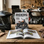 Riviste di moto su tavolo in legno con casco e guanti da motociclista. Sullo sfondo una moto con attrezzi di meccanica