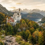 Inquadratura di un viaggio in Germania, che mostra un castello immerso in un vibrante scenario autunnale nelle Alpi Bavaresi.
