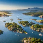 Panoramica aerea di un viaggio in Svezia in un arcipelago svedese con isole verdi, tipiche case rosse in legno, barche in movimento e montagne sullo sfondo.