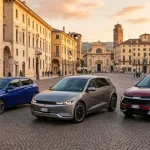 Inquadratura granangolare e fotorealistica di tre auto coreane moderne parcheggiate fianco a fianco in una piazza italiana.