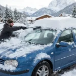 Automobilista pulisce auto da una abbondante precipitazione nevosa, confermando le previsioni di neve in montagna.