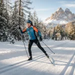 Atleta impegnata in una allenamento di sci di fondo su un anello in una pineta assolata.