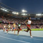 Atleti impegnati una gara delle Olimpiadi su pista di atletica con pubblico sugli spalti, bandiere di diverse nazioni.
