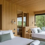 Eco-resort integrato nel bosco, vetrate che riflettono la natura, arredamento minimal in legno naturale, concetto di hotel sostenibili e lusso green.