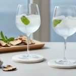 Bicchieri eleganti con bevande adattogene funzionali, ghiaccio cristallino, erbe e funghi reishi sullo sfondo
