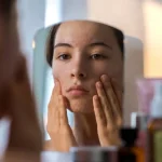 Adolescente con acne e brufoli sul viso si guarda allo specchio