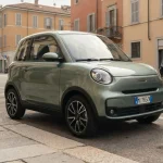 Moderna microcar compatta a quattro ruote parcheggiata in una strada urbana italiana, vista a tre quarti frontale.