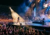 Un concerto tipico di gruppi rock famosi con musicisti scalmanati sul palco e pubblico entusiasta.